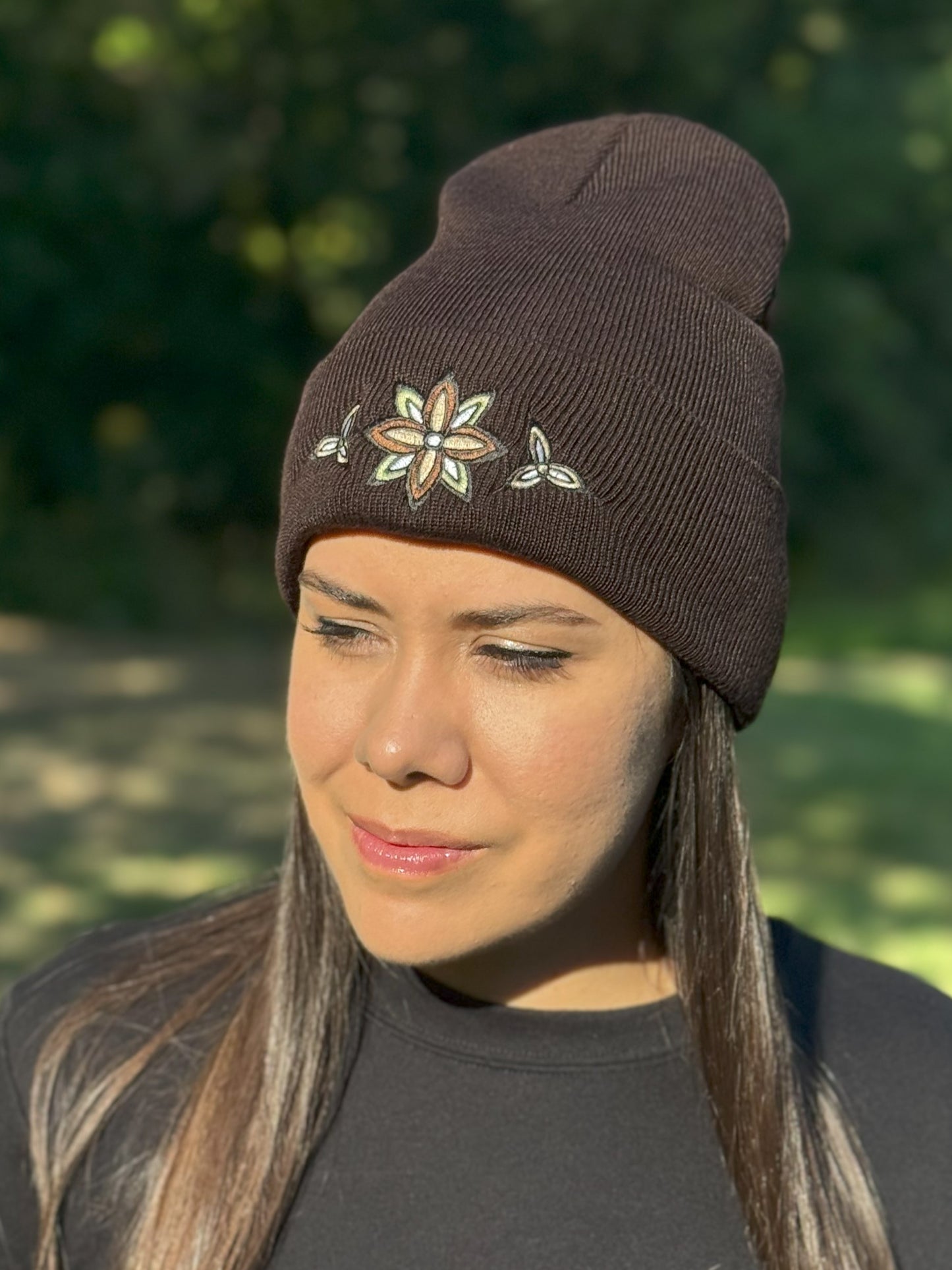 A woman wearing a dark brown rib knit toque with a stylized flower embroidery in neutral colours