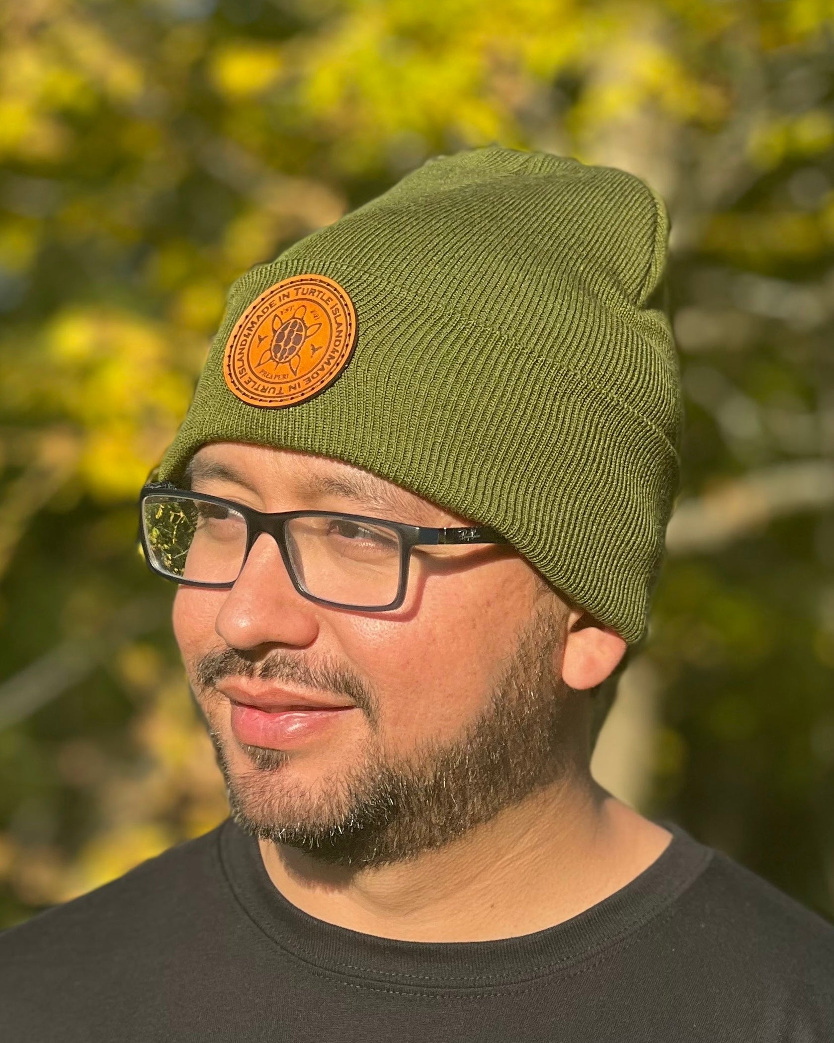 A man wearing an olive green toque with a leather patch with and engraving of a turtle with the words "Made in Turtle Island" around it.