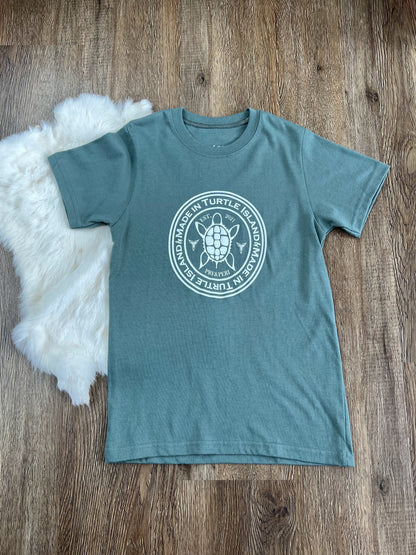 Flat lay picture of a sage green t-shirt with white screen print of a stylized turtle with the words "Made in Turtle Island" around it.