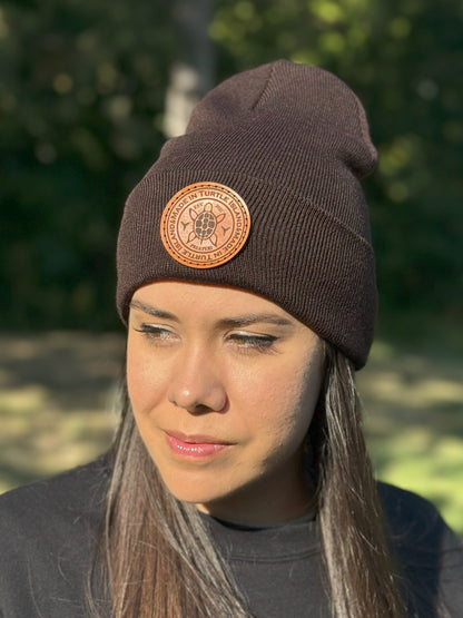 A woman wearing a dark brown toque with a leather patch with and engraving of a turtle with the words "Made in Turtle Island" around it.
