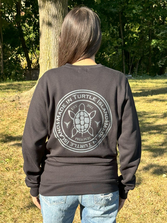 Back view of a woman wearing a black crewneck sweatshirt with grey print of a stylized turtle with the words "Made in Turtle Island" around it