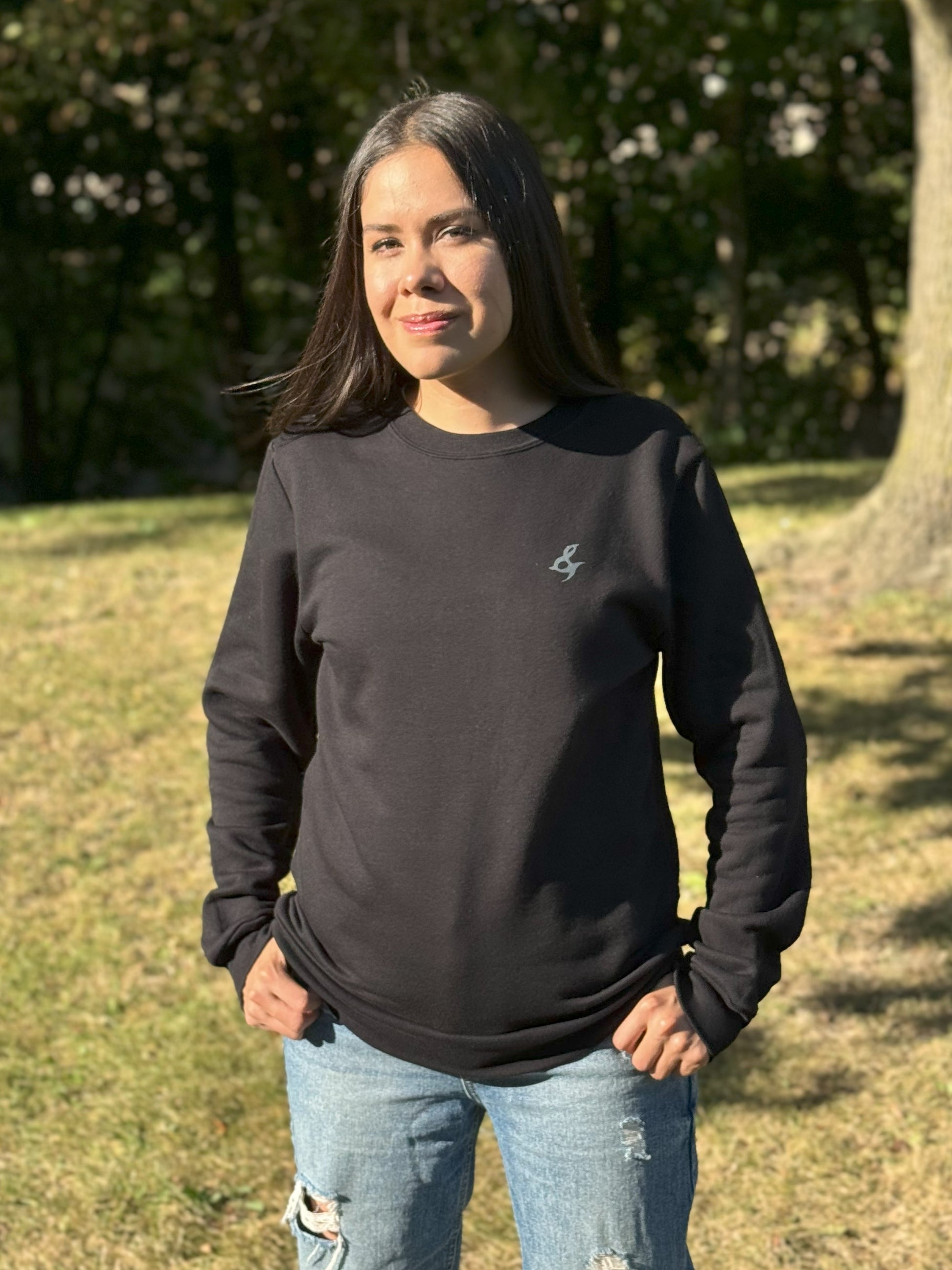 A woman wearing a black crewneck sweatshirt with a small stylized ampersand on the left chest. 