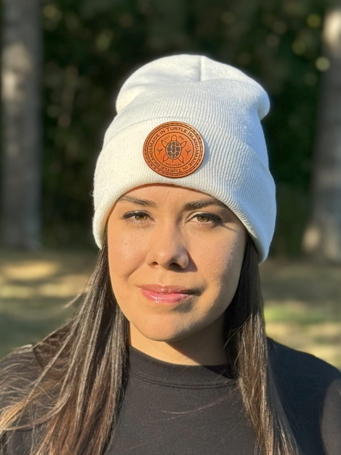 A woman wearing an off-white toque with a leather patch with and engraving of a turtle with the words "Made in Turtle Island" around it.