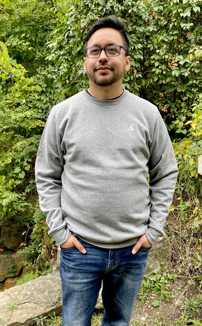 A man wearing a grey crew neck sweatshirt with a stylized ampersand logo on the chest