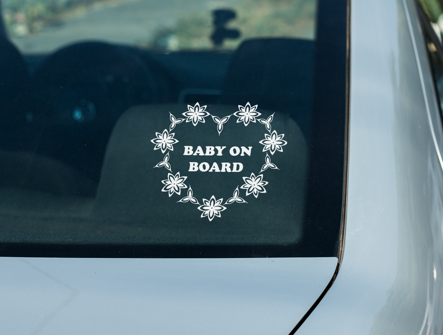 A white decal with the words "Baby on Board"  surrounded by a heart made up of stylized flower motifs