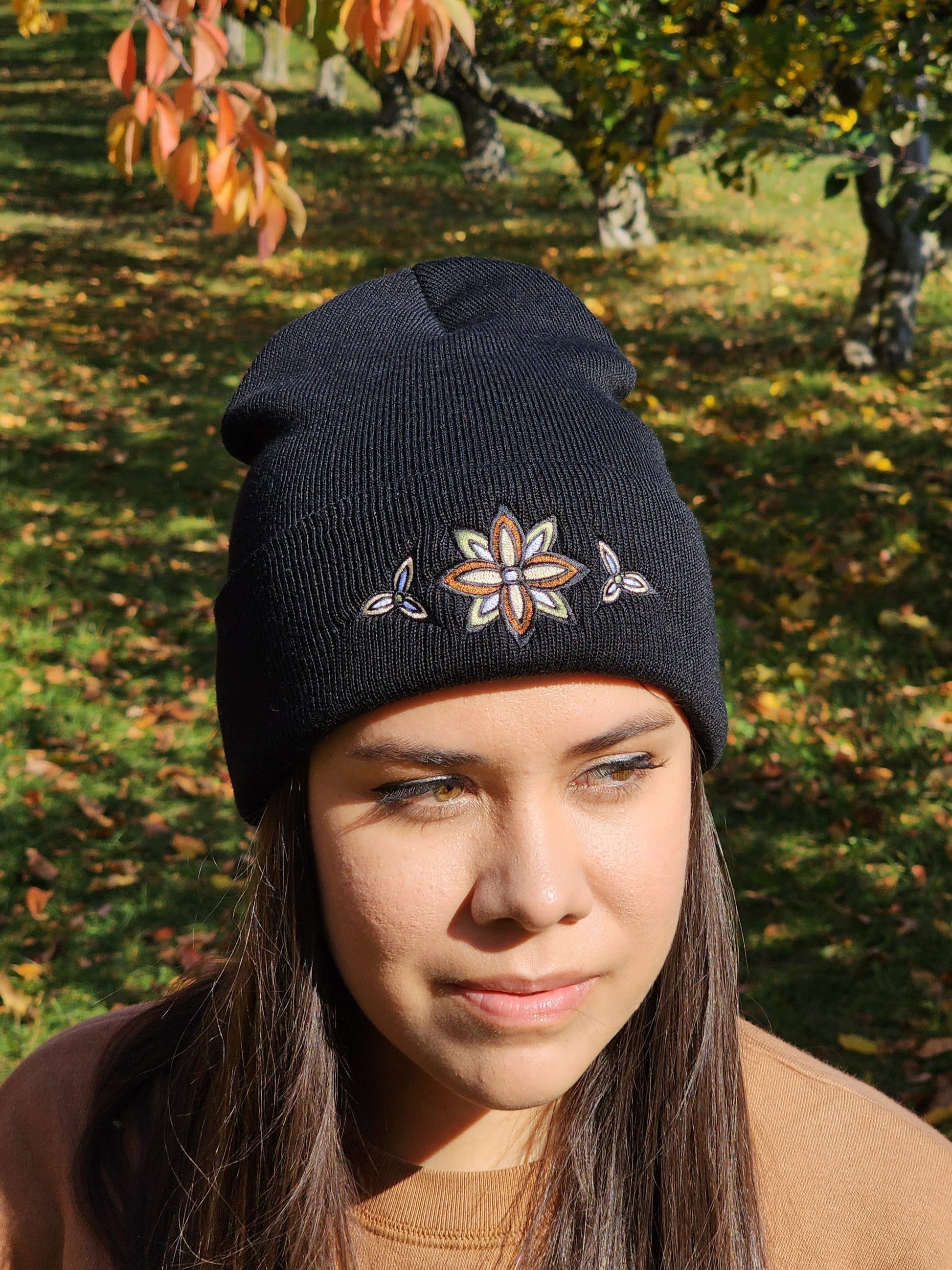 A woman wearing a black rib knit toque with a stylized flower embroidery in neutral colours