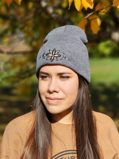 A woman wearing a charcoal rib knit toque with a stylized flower embroidery in neutral colours