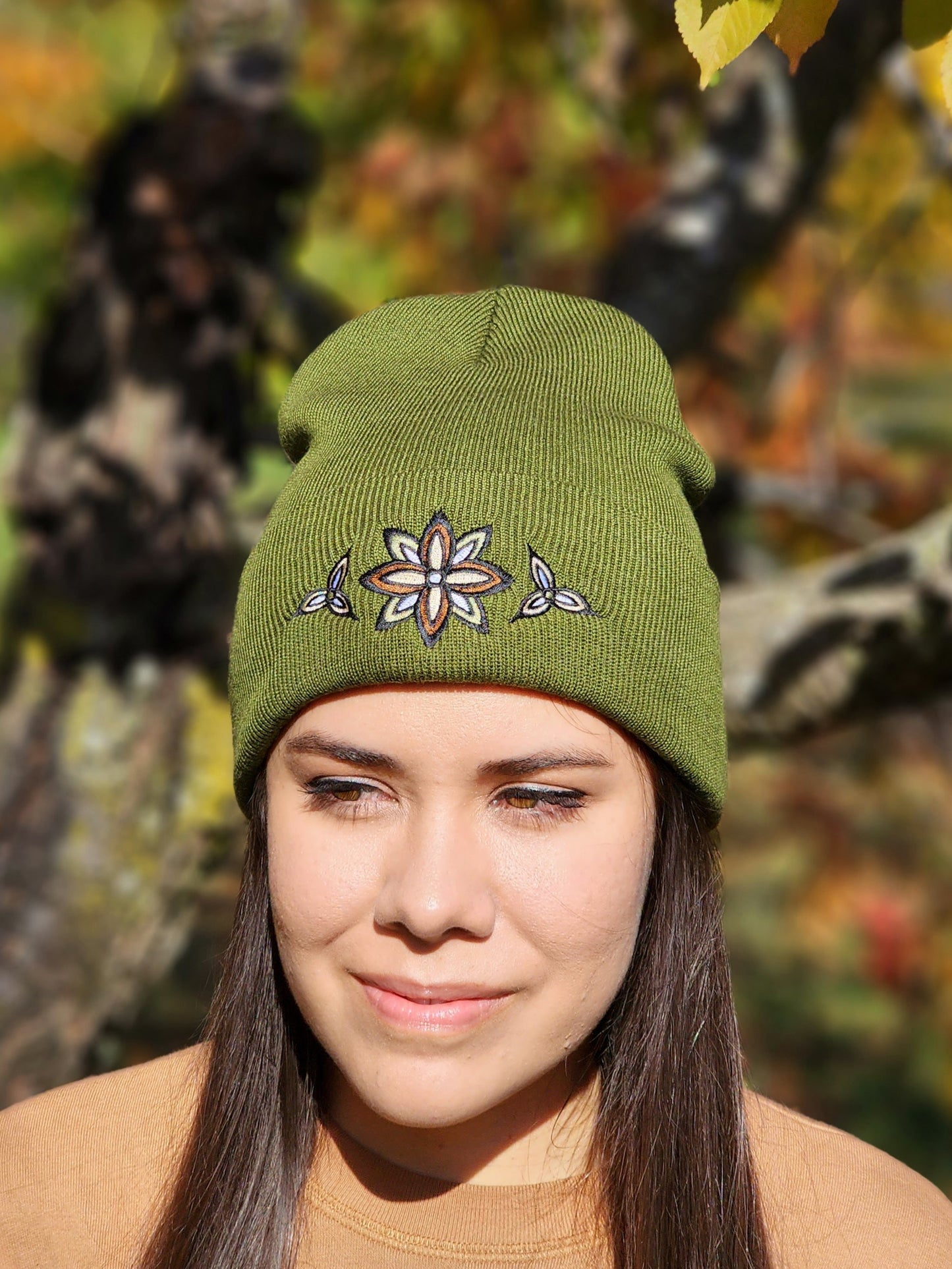 A woman wearing an olive green rib knit toque with a stylized flower embroidery in neutral colours