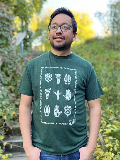 A man wearing a forest green t-shirt with a white print of stylized animal and human footprints encased by a rectangle formed by the words "Wea are all related. Caring for People. Animals, Planet."
