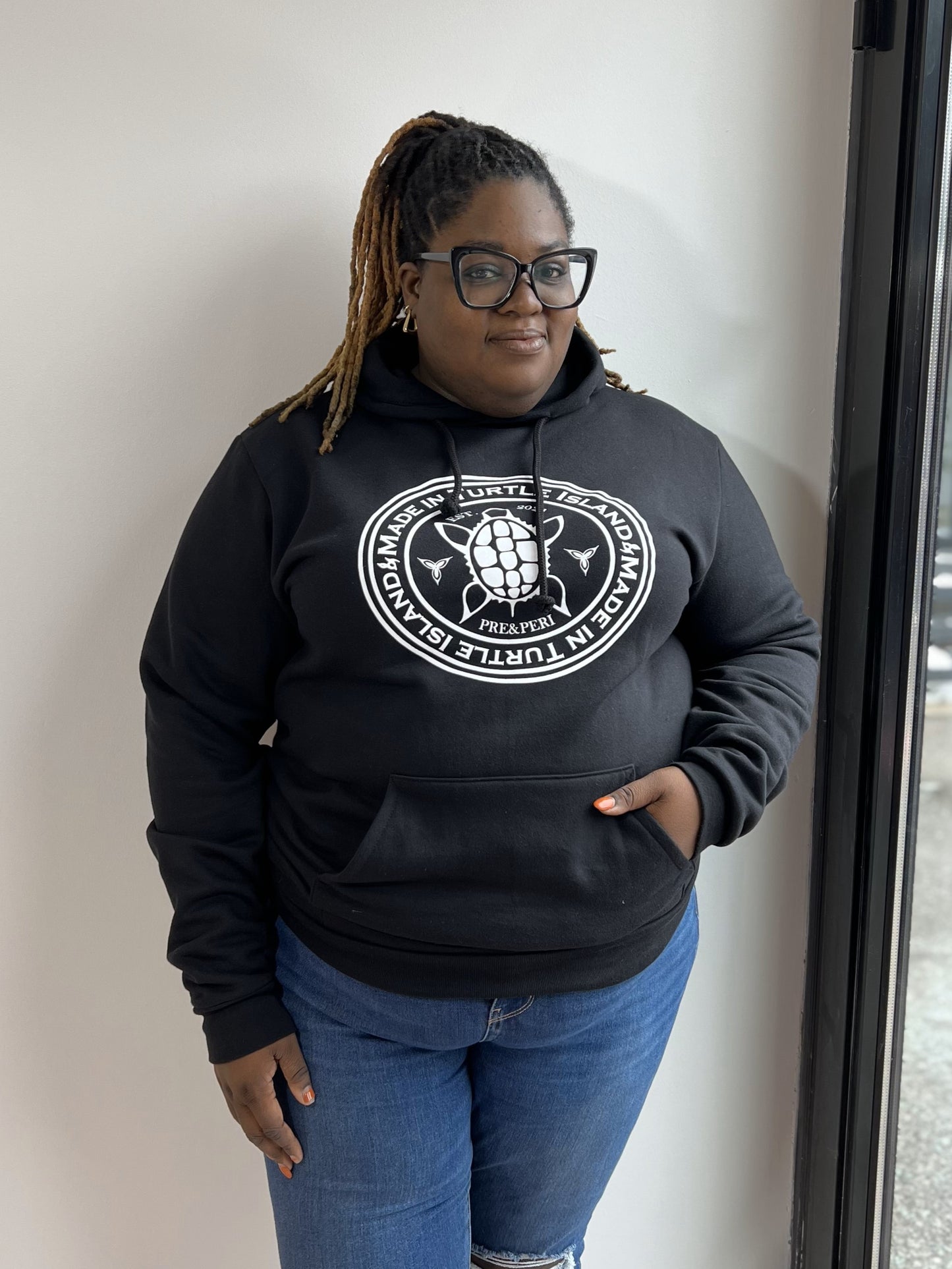 A woman wearing a black hoodie with a white print of a turtle with words "Made in Turtle Island" around it.