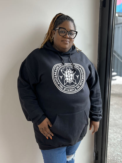 A woman wearing a black hoodie with a white print of a turtle with words "Made in Turtle Island" around it.