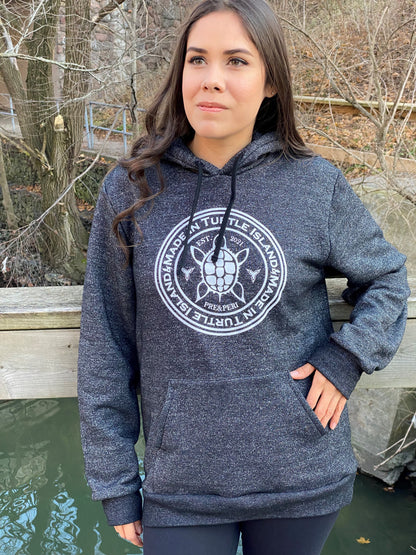 A woman wearing a salt and pepper hoodie with a white graphic featuring a stylized turtle with the words "Made in Turtle Island" around it.