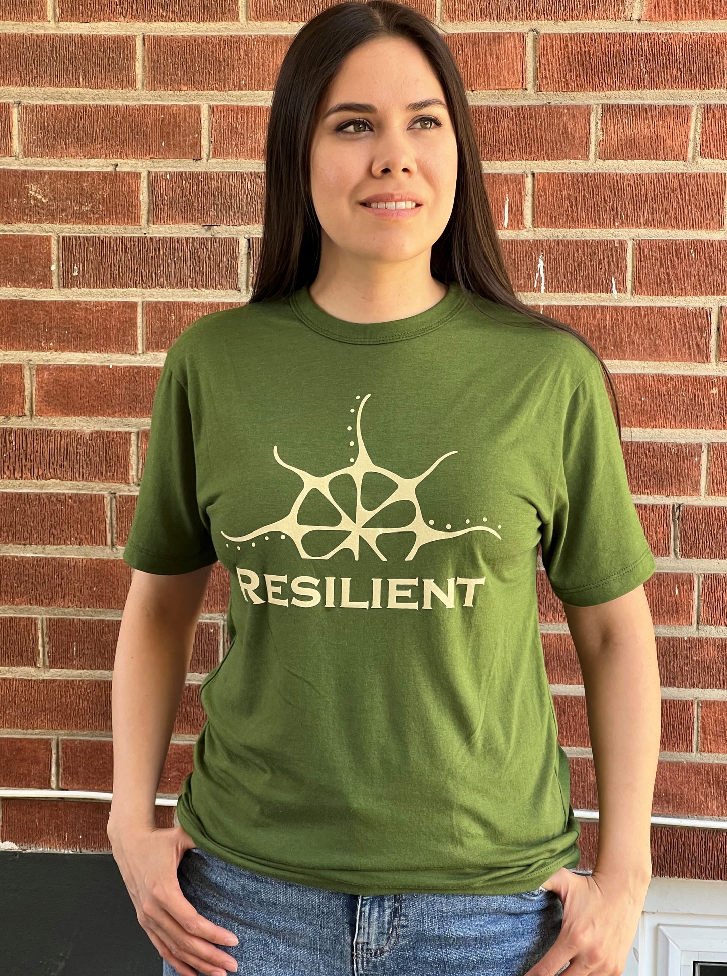 A woman wearing a green t-shirt with a pale yellow print that says "Resilient" under a stylized rising sun.