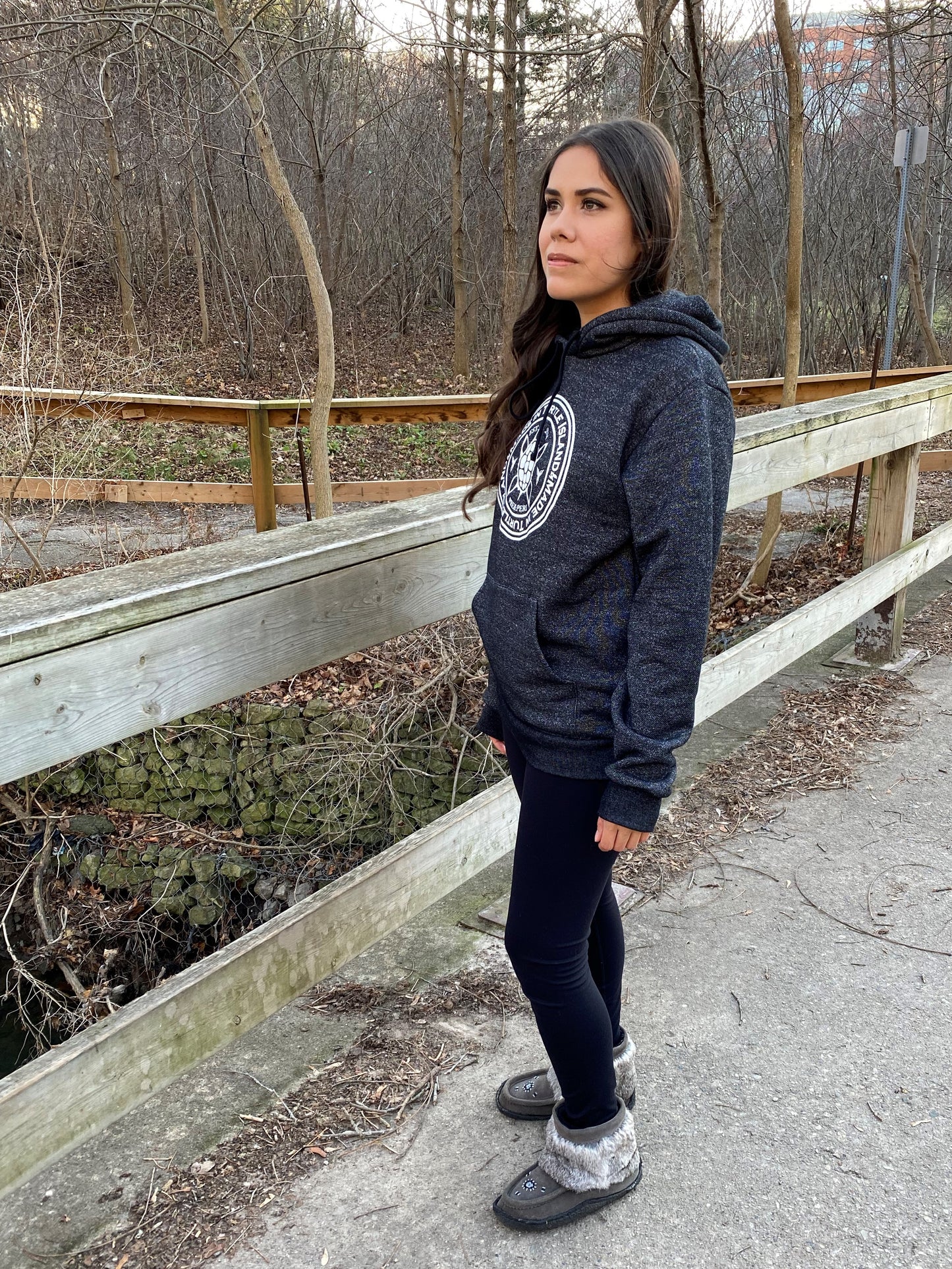Angled side view of a woman wearing salt and pepper hoodie with round white graphic and beaded moccasin-style boots 
