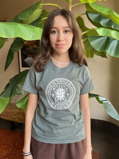 A girl wearing a forest green t-shirt with a white print of a turtle in a circle with the words "Made in Turtle Island" around it.